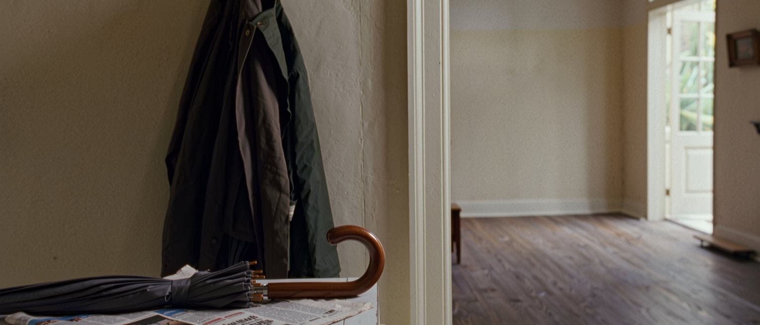 a kitchen counter with an umbrella left open to dry, a raincoat on the hook beside it and a folded weather page of the paper on the worktop, the window soft behind