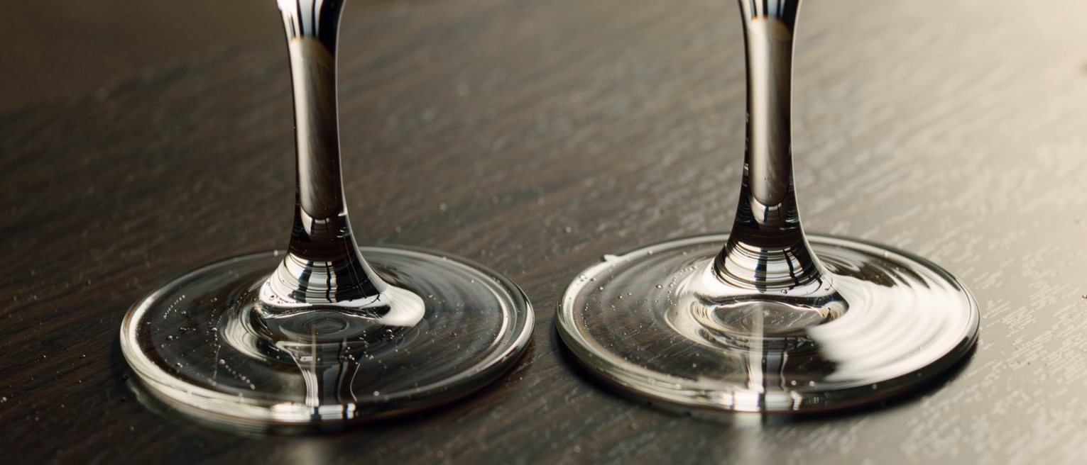 two wine glasses standing apart on a dark table, each in its own small circle of moisture
