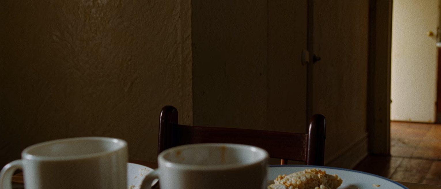 a kitchen table seen close with two cups and a plate of something half eaten between them, one chair pulled out at an angle