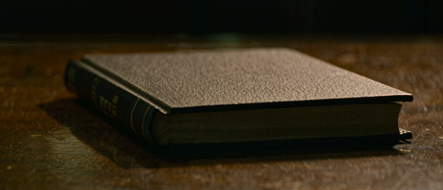 a thick book bound in dark cloth, closed and squared on a table, its page edges cut clean and even