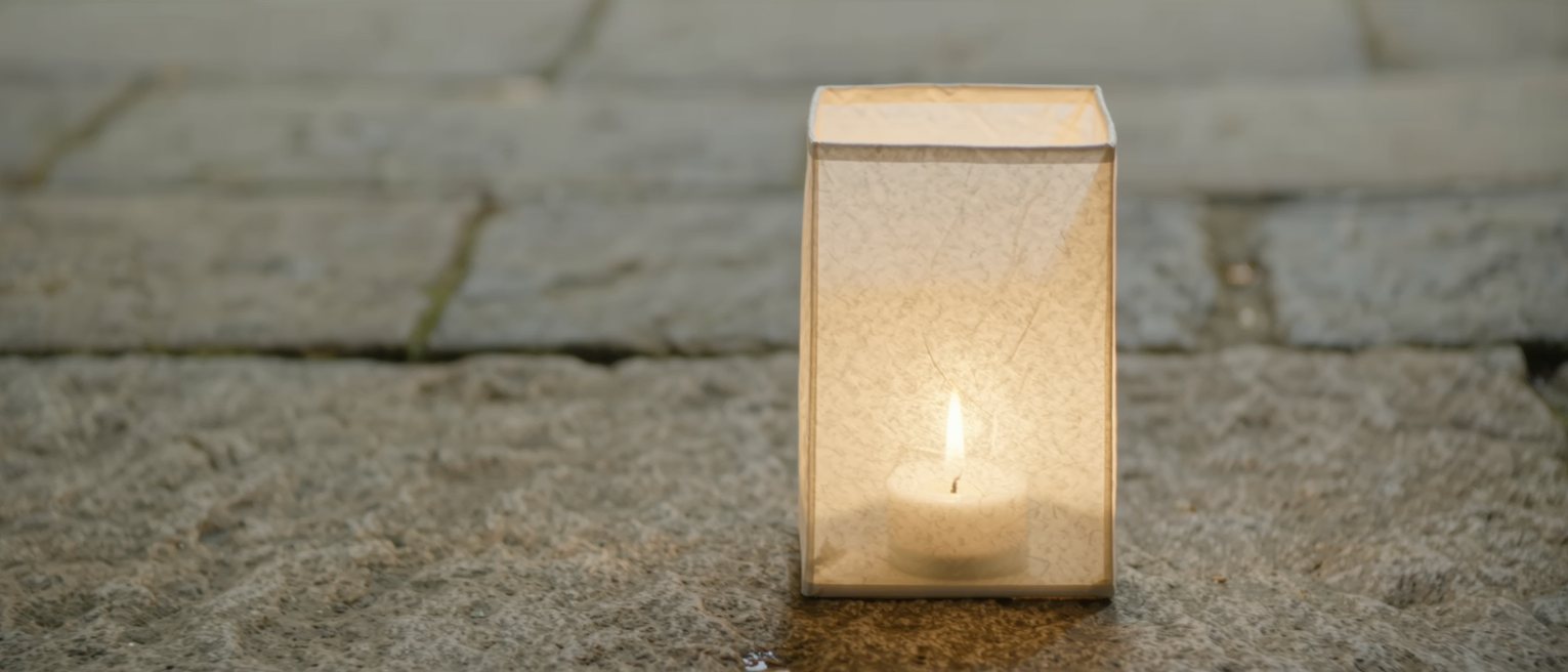 a plain paper lantern glowing from the candle inside it, the paper unmarked, standing on a stone step