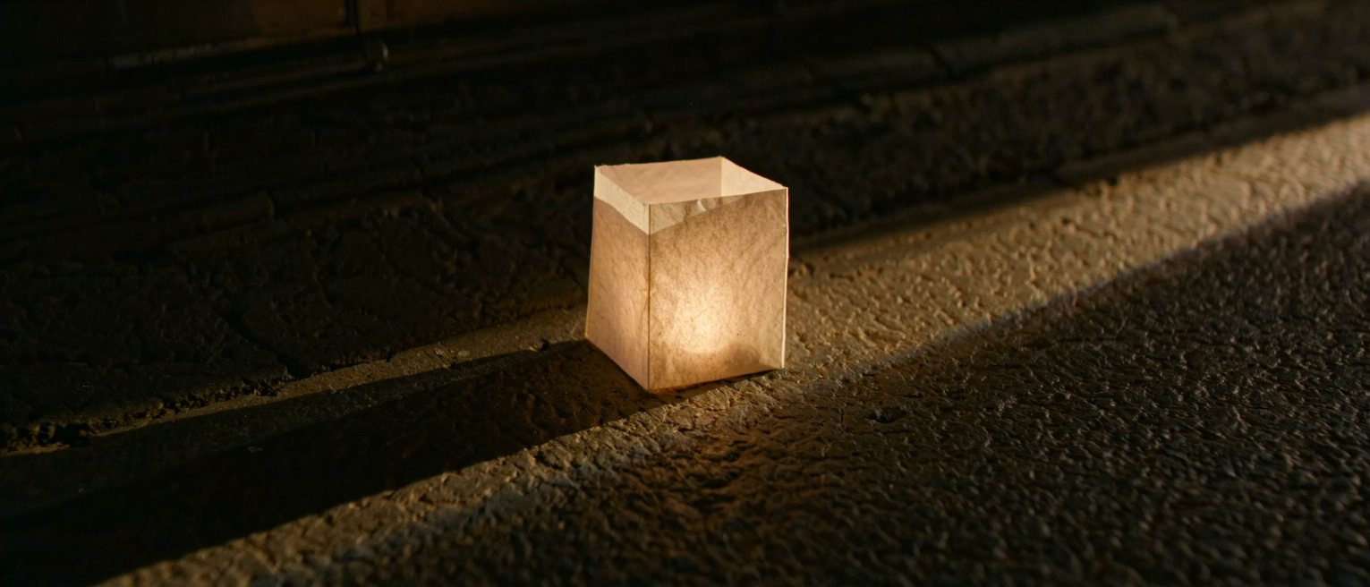 a plain paper lantern glowing from the candle inside it, the paper unmarked, standing on a stone step