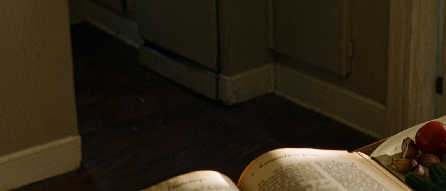 a kitchen with a cookbook open at a page gone soft and splashed with use, the same ingredients set out in the same order