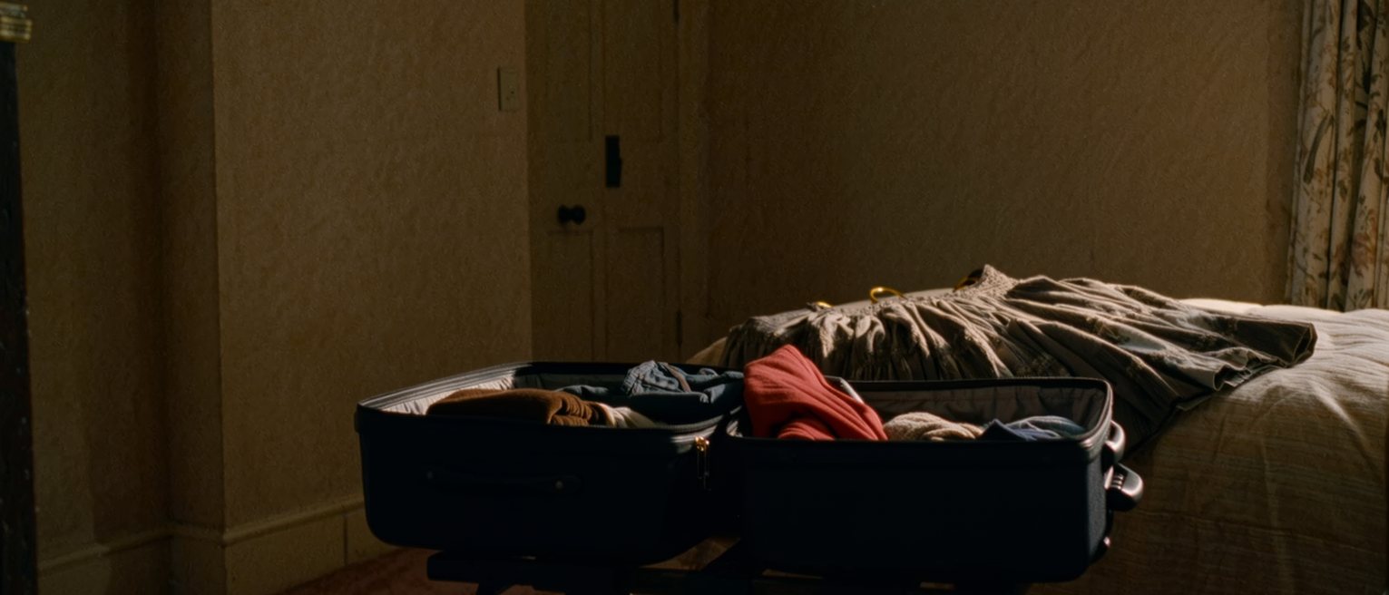 an unfamiliar bedroom with a suitcase open on the luggage stand and a dress laid out on the bed that would never be worn at home