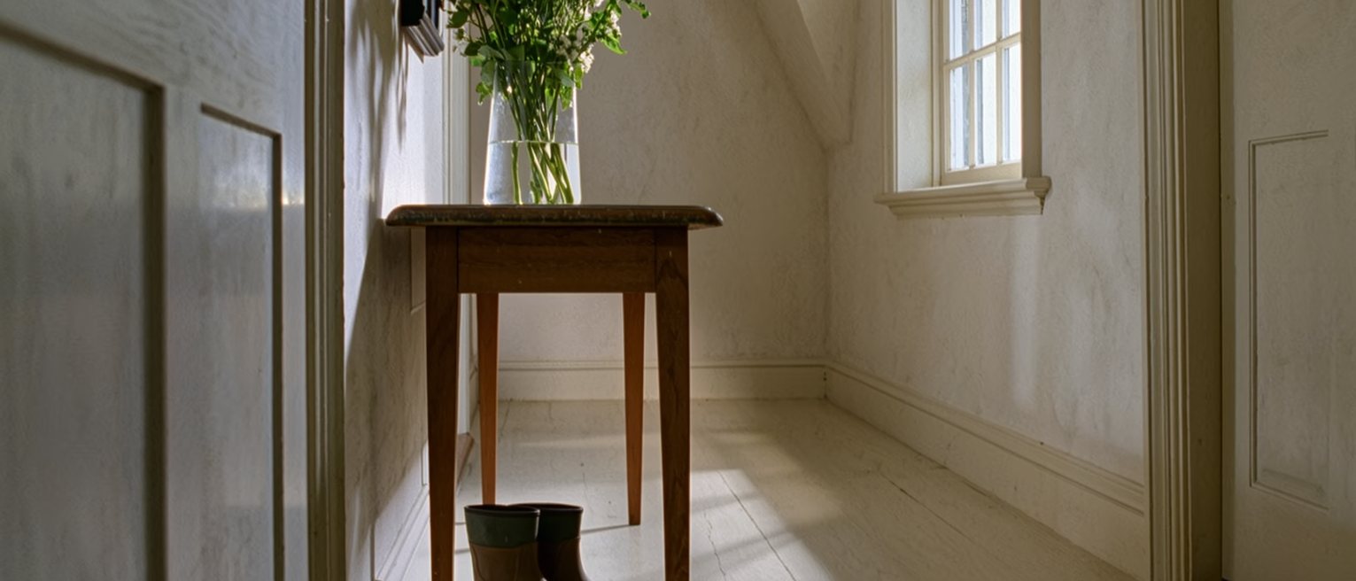 a hall table with a bunch of flowers put in water and, beside them, the same pair of muddy boots left where they always are