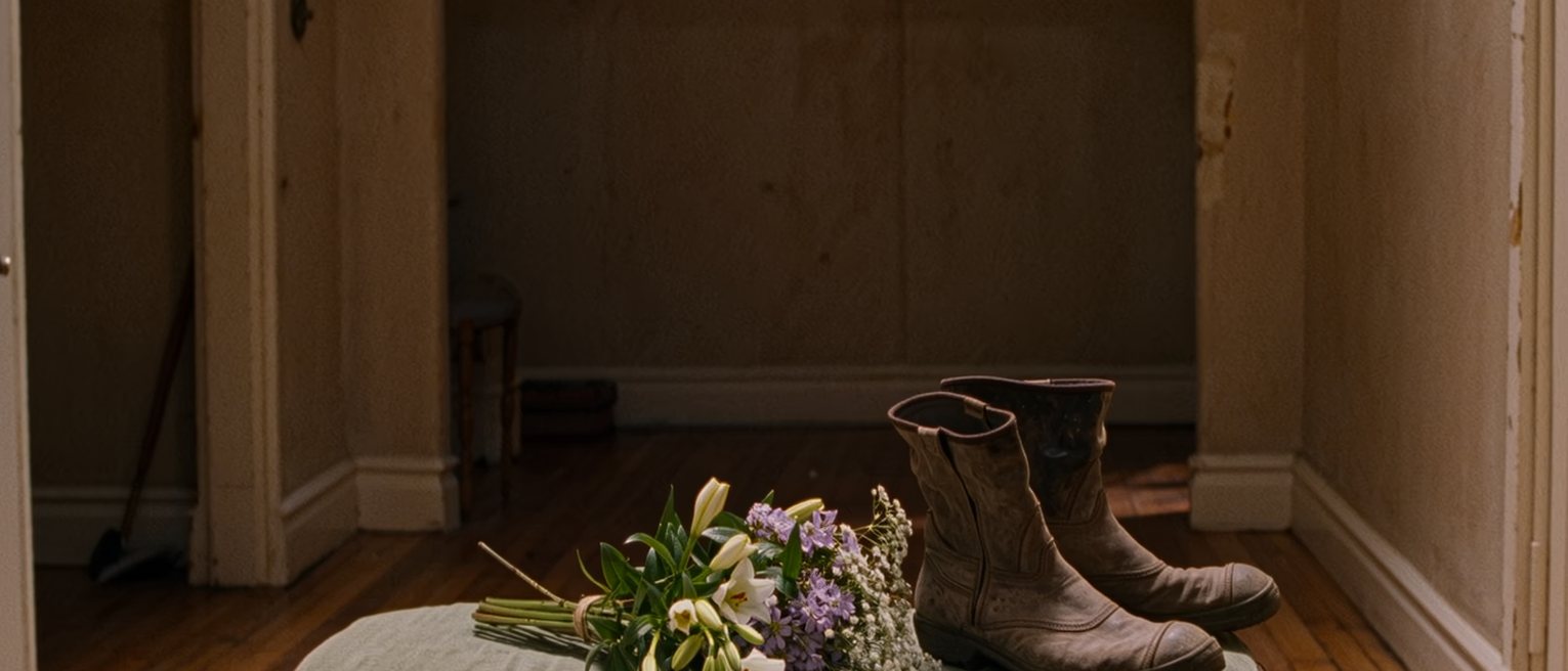 a hall table with a bunch of flowers put in water and, beside them, the same pair of muddy boots left where they always are