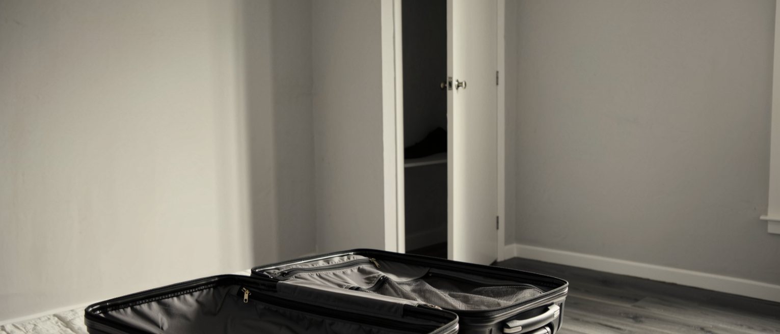 a bedroom with a suitcase open on the bed and nothing yet in it, a wardrobe door standing open