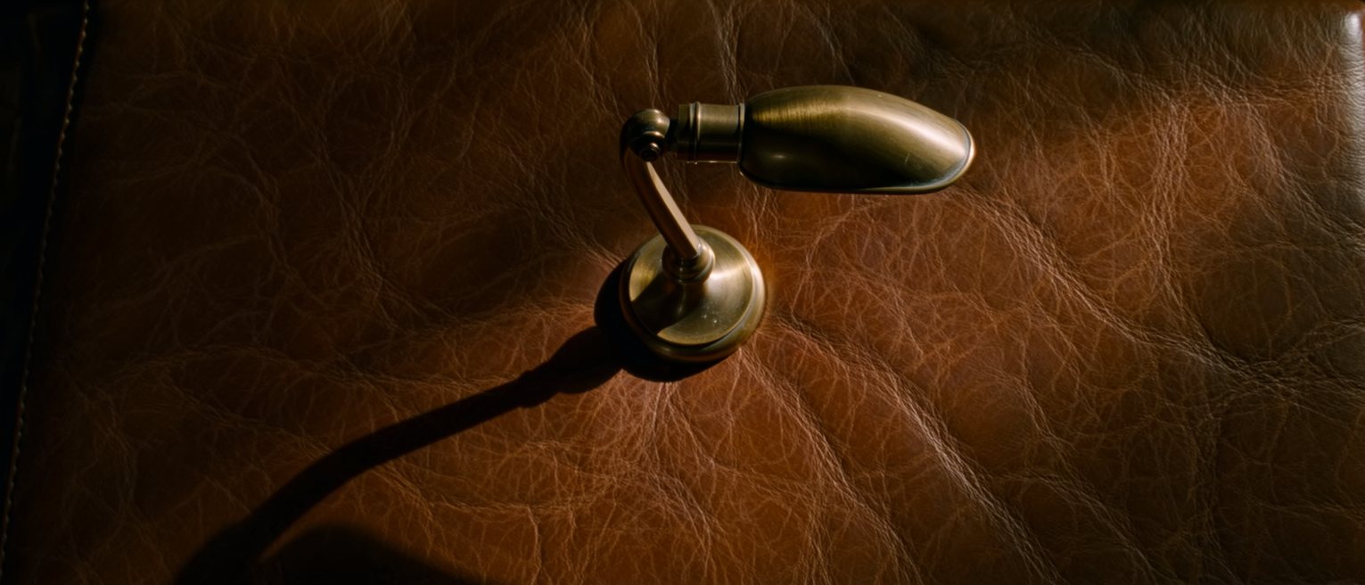 a brass desk lamp with its shade tilted down over a leather desktop