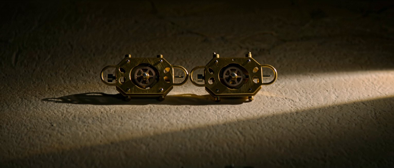 two brass pendulum movements side by side, bare gearwork and bob, their pendulums swinging out of step