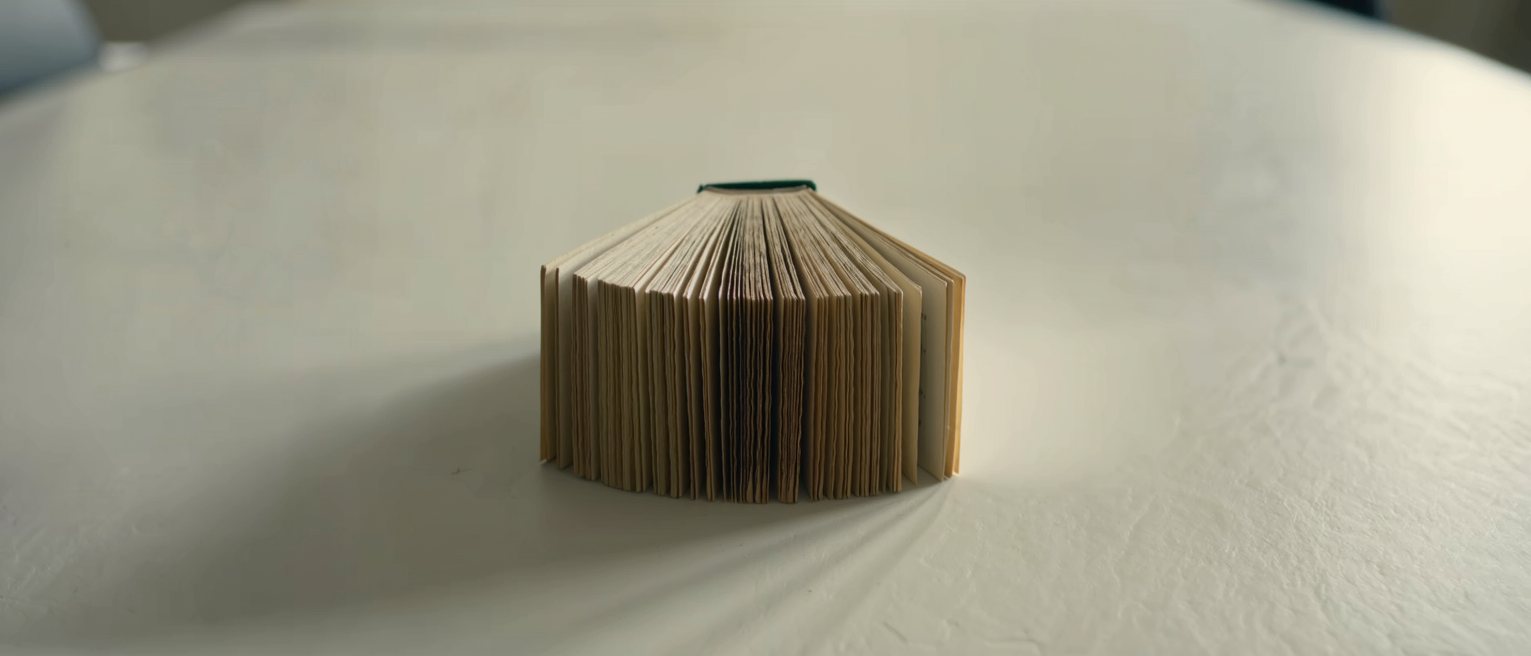 a paperback book lying open and inverted on a table, the spine deeply creased from reading