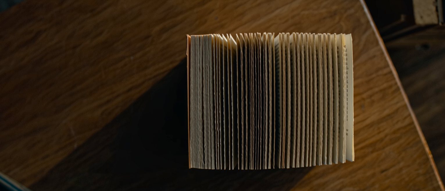 a paperback book lying open and inverted on a table, the spine deeply creased from reading