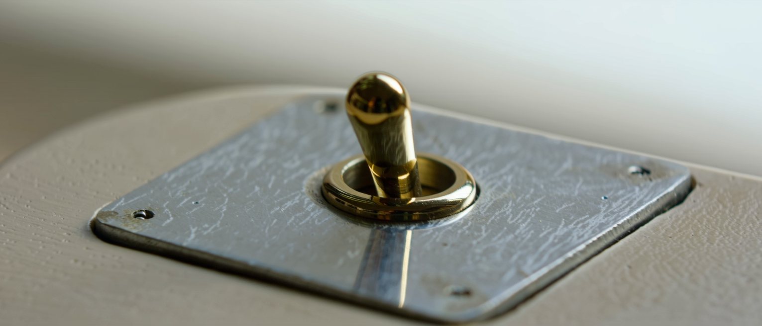 a single brass toggle switch on a mounting plate, thrown hard to one side