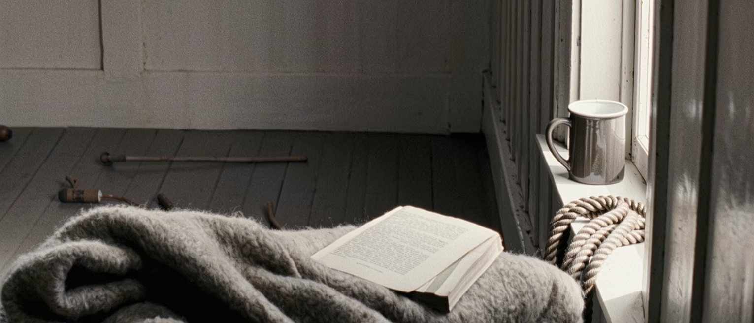 a bunkhouse seen close with a horse blanket folded on the bed, a length of rope coiled on the sill beside a mug, a law textbook borrowed and unopened, the window onto the flat land soft behind