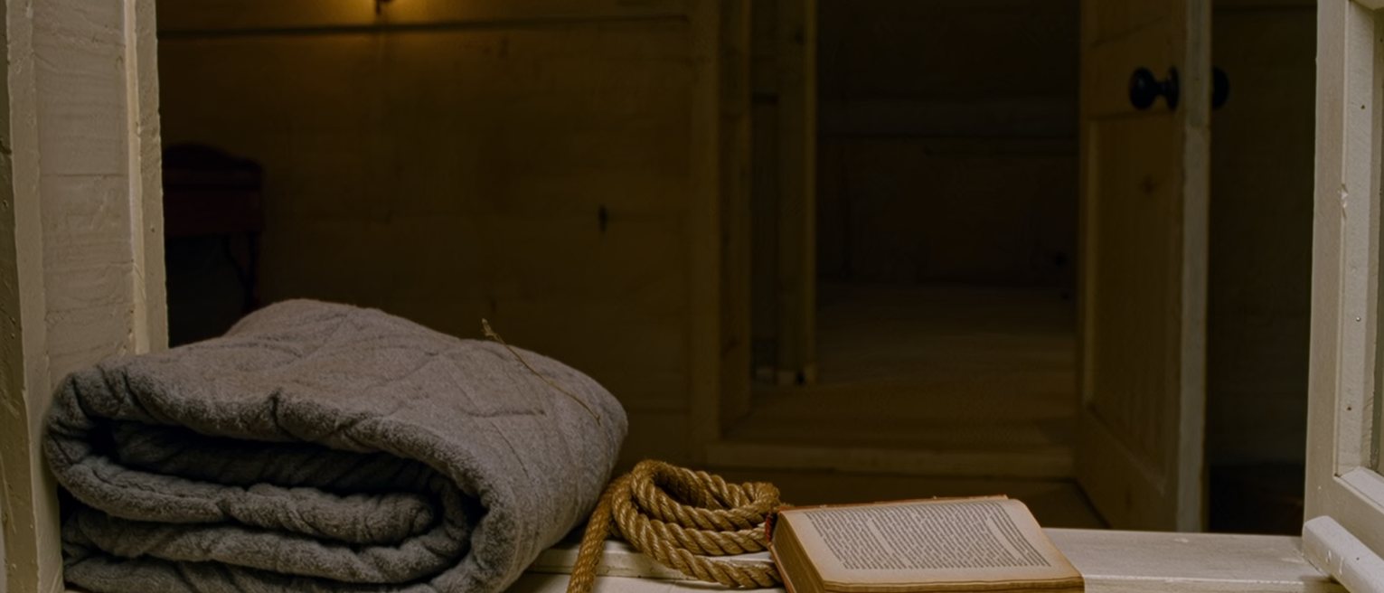 a bunkhouse seen close with a horse blanket folded on the bed, a length of rope coiled on the sill beside a mug, a law textbook borrowed and unopened, the window onto the flat land soft behind