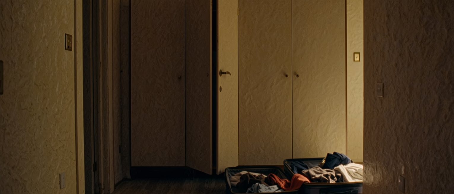 a bedroom with two suitcases open side by side and the contents already mixed, one wardrobe shared down the middle