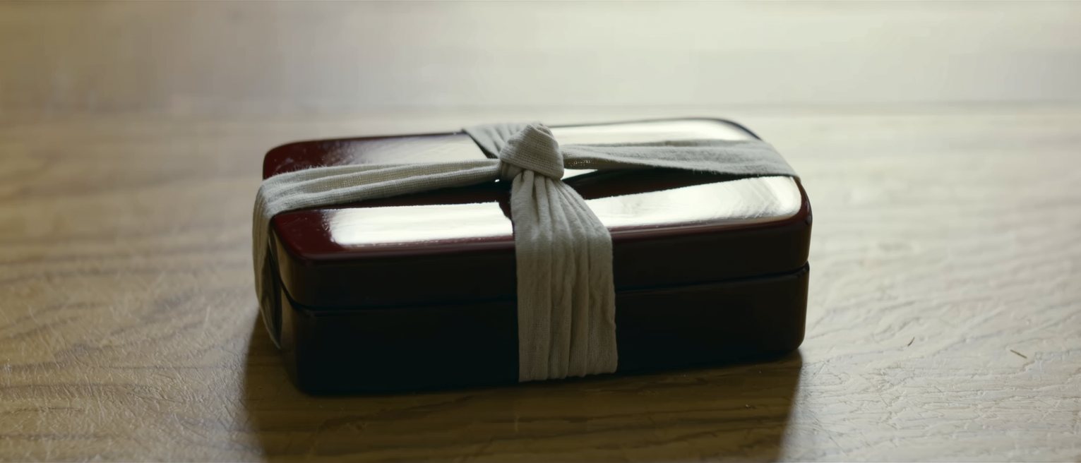 a lacquer lunch box tied up in a plain cloth, the knot squared