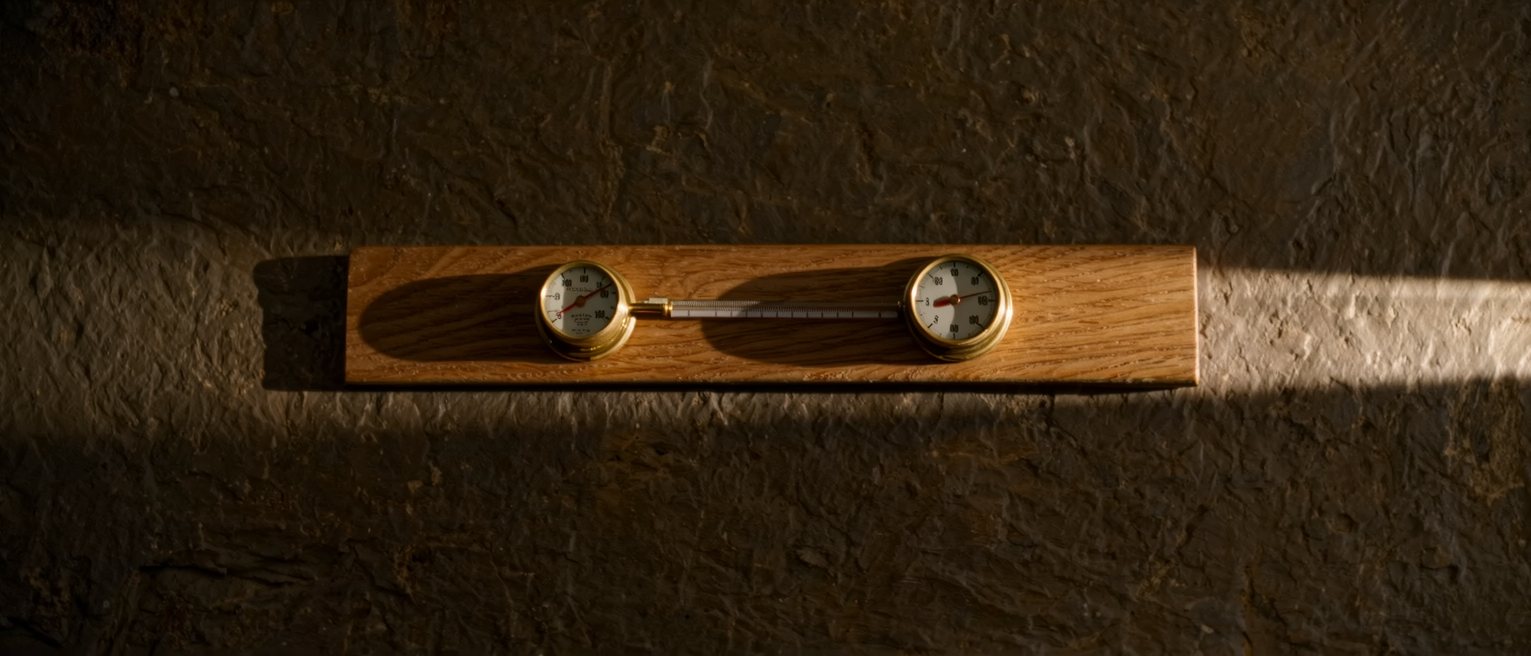 a brass thermometer and a brass hygrometer mounted side by side on an oak board, both dials plain and unnumbered