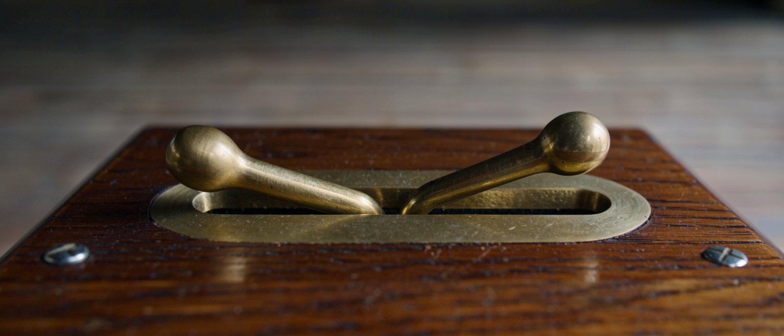 the two brass levers of a throttle quadrant on a varnished timber console, one pushed forward and the other drawn back
