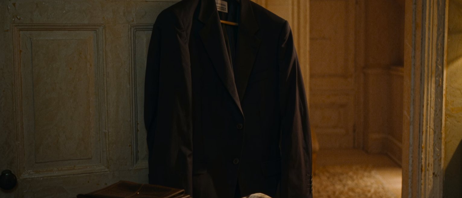 a bedroom where a suit is hung ready on the wardrobe door and a silk slip has been folded and put away on a shelf