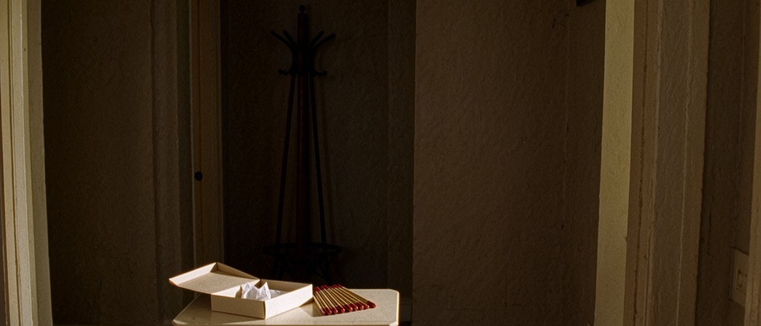 a hall table seen close with an empty gift box, its lid off and tissue paper folded inside, and beside it a tidy row of identical pens, the coat rack soft behind