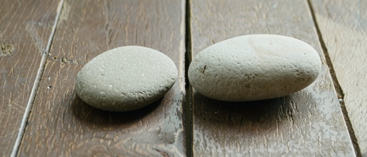 two smooth river stones set down beside each other on a worn wooden table, close but not touching