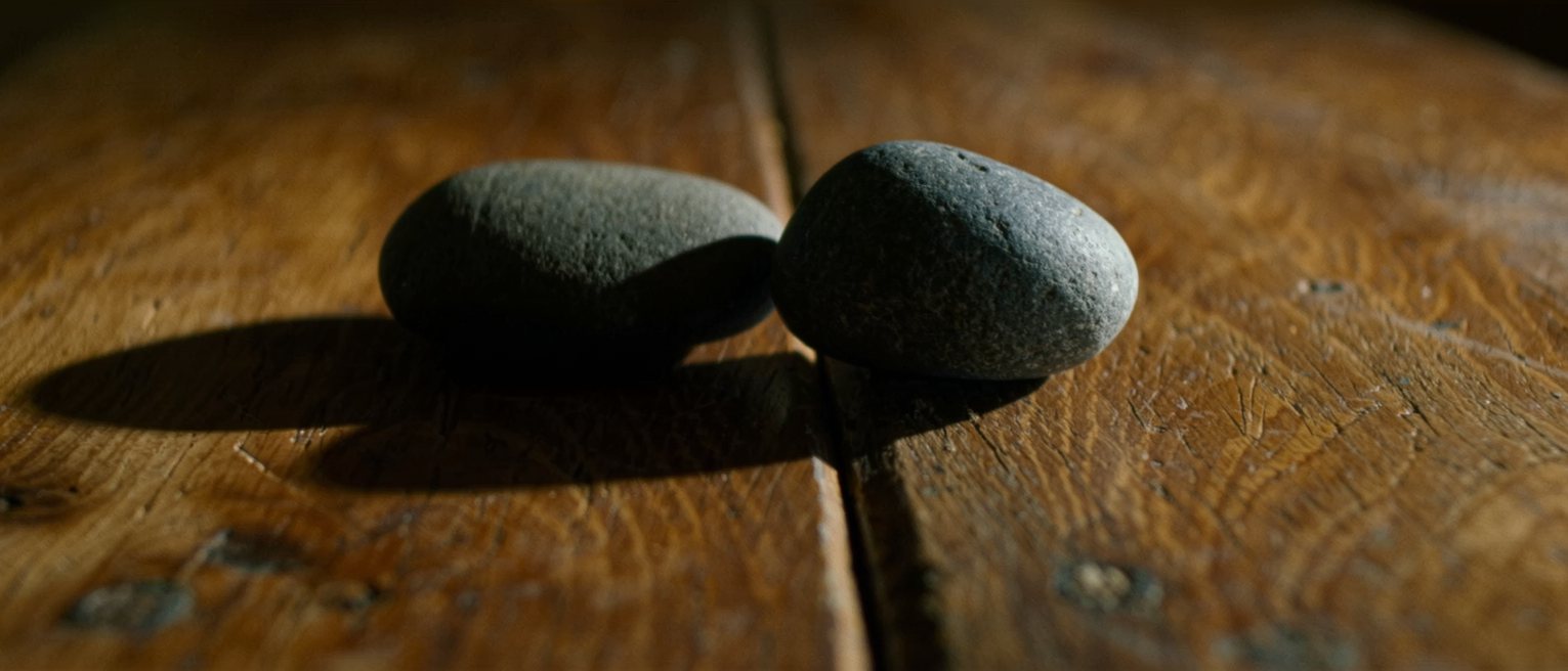 two smooth river stones set down beside each other on a worn wooden table, close but not touching