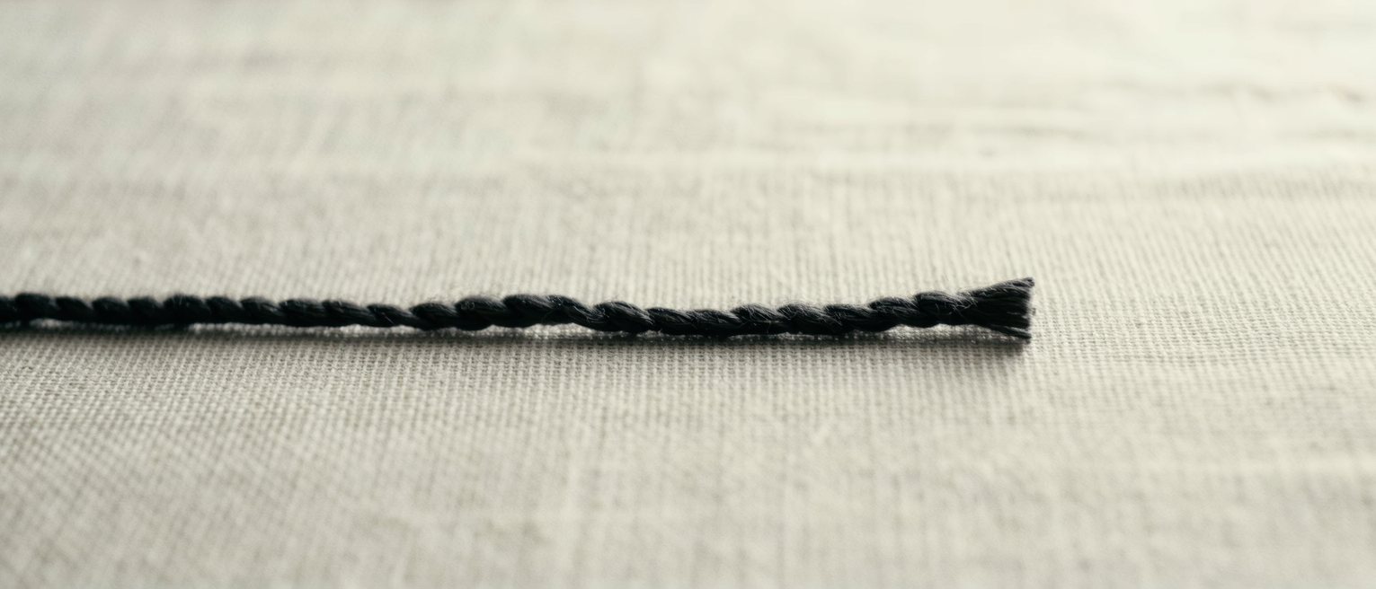 a single length of dark silk thread laid straight across pale linen, cut clean and square at one end