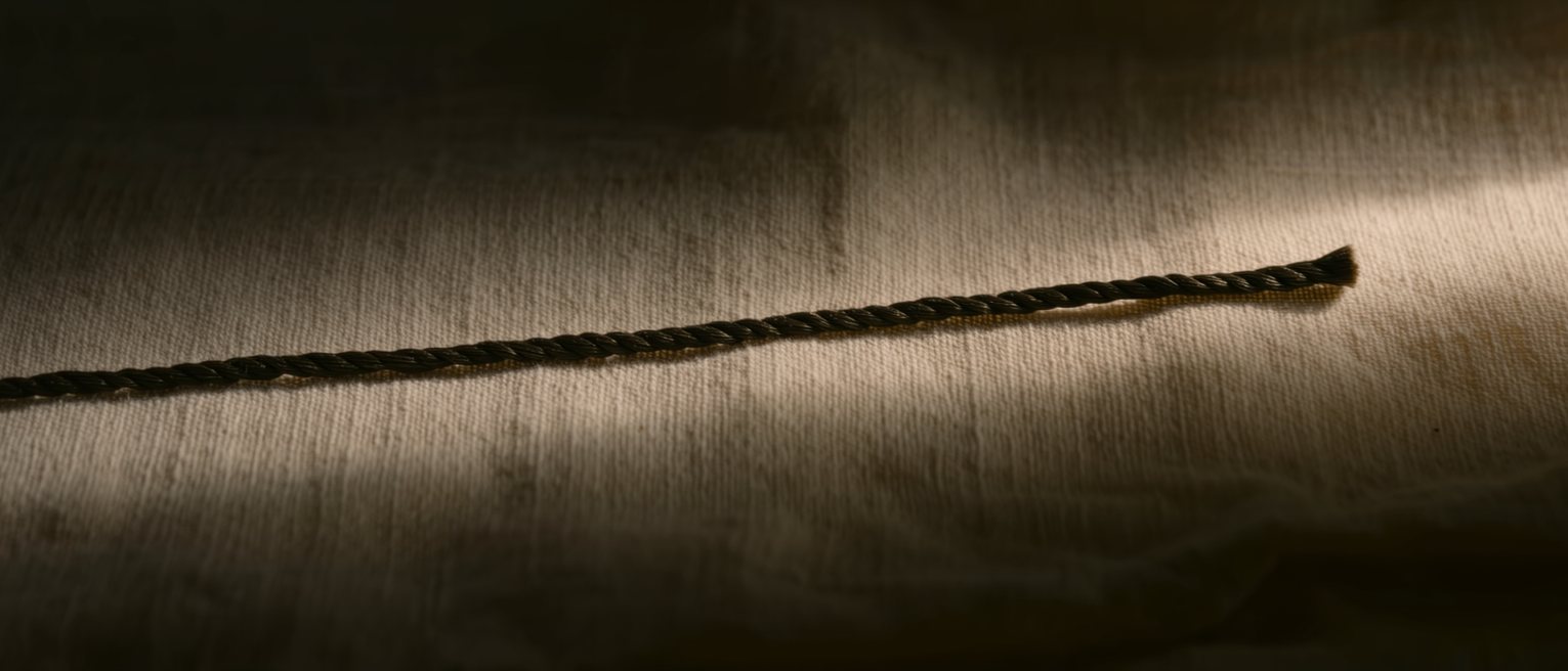 a single length of dark silk thread laid straight across pale linen, cut clean and square at one end