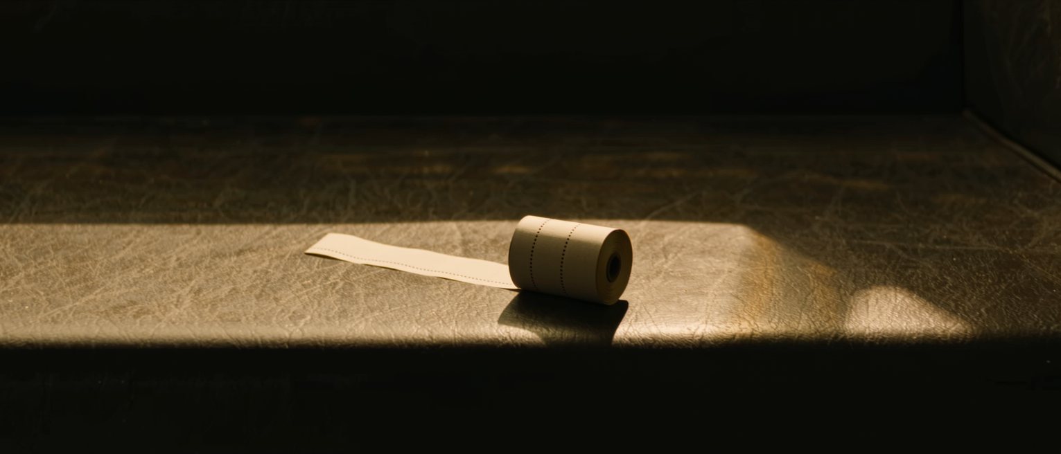 a long strip of blank paper tickets folded into a concertina stack on a bench, every ticket identical and unprinted