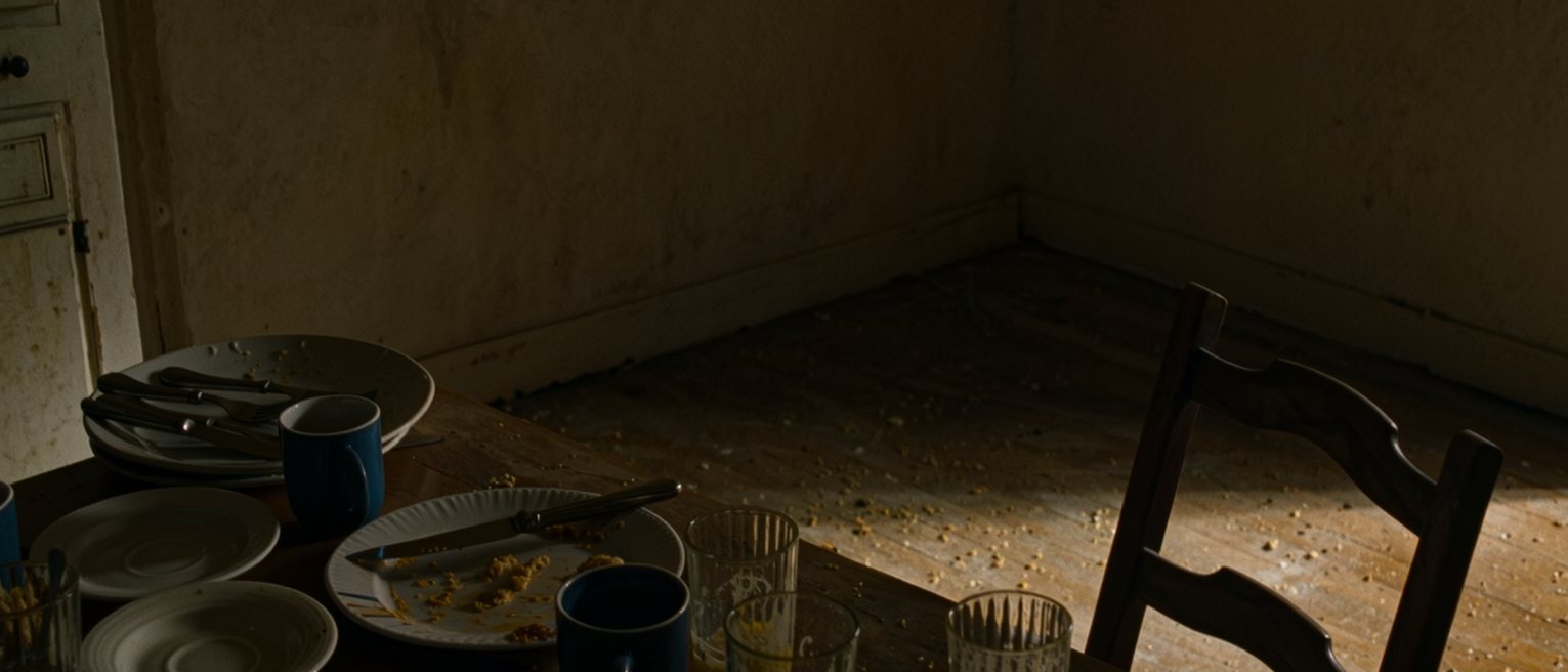 a kitchen with the breakfast things for four left unwashed for days, the table still laid for four, one chair pulled out