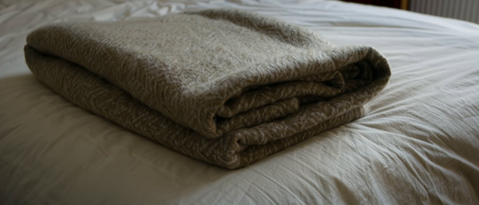 a heavy wool blanket folded once and left at the foot of a made bed