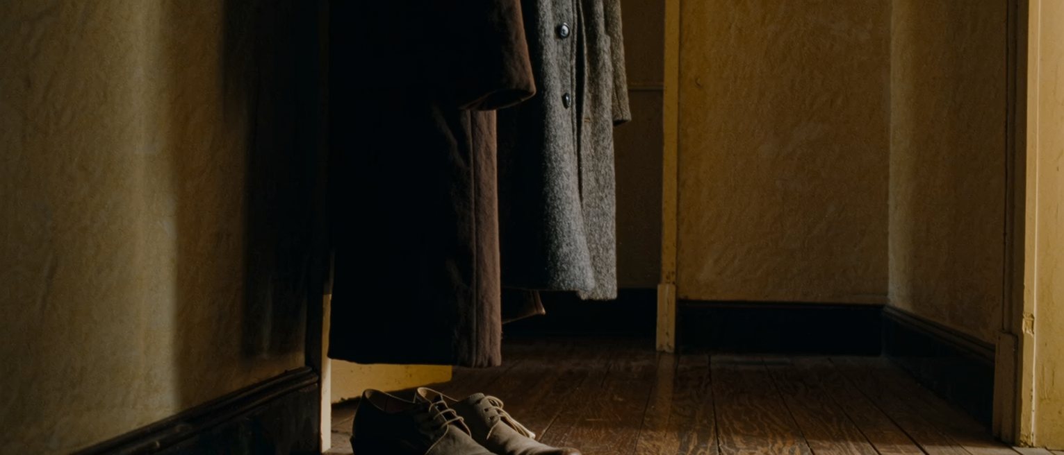 a hall with one good coat on the hook and one pair of good shoes beneath it, both kept, both dusted, neither worn for a season