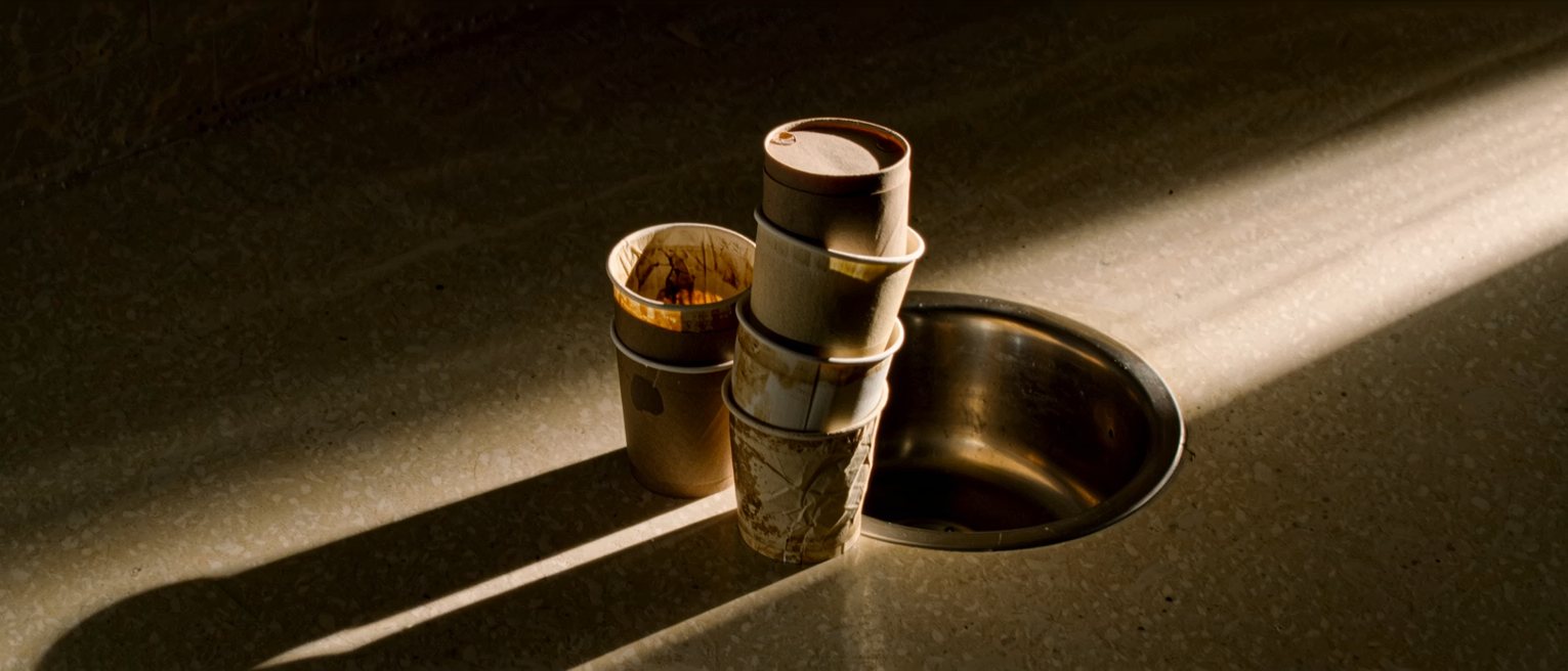 a stack of used coffee cups left beside a sink, not one of them rinsed