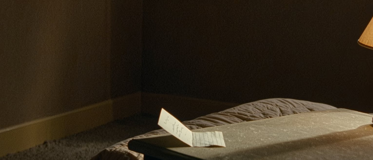 a bedside table with a folded note propped against the lamp, and the far side of the bed turned down ready