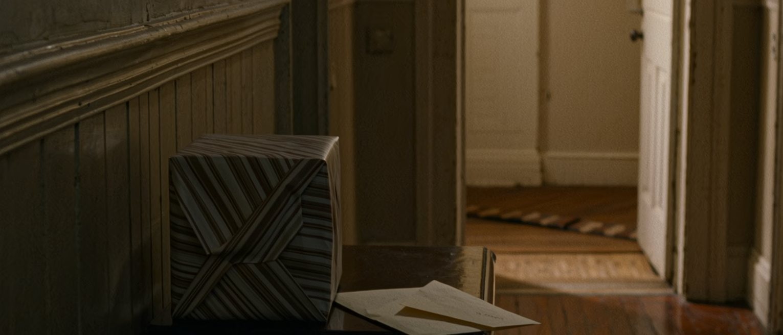 a wrapped gift set down on a hall table beside an unopened letter, its ribbon still perfect