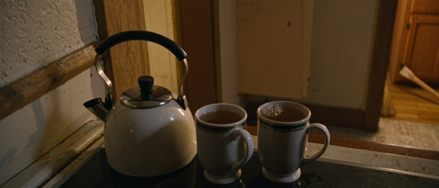 a kitchen where two mugs of tea have been made and one has gone cold untouched beside the kettle