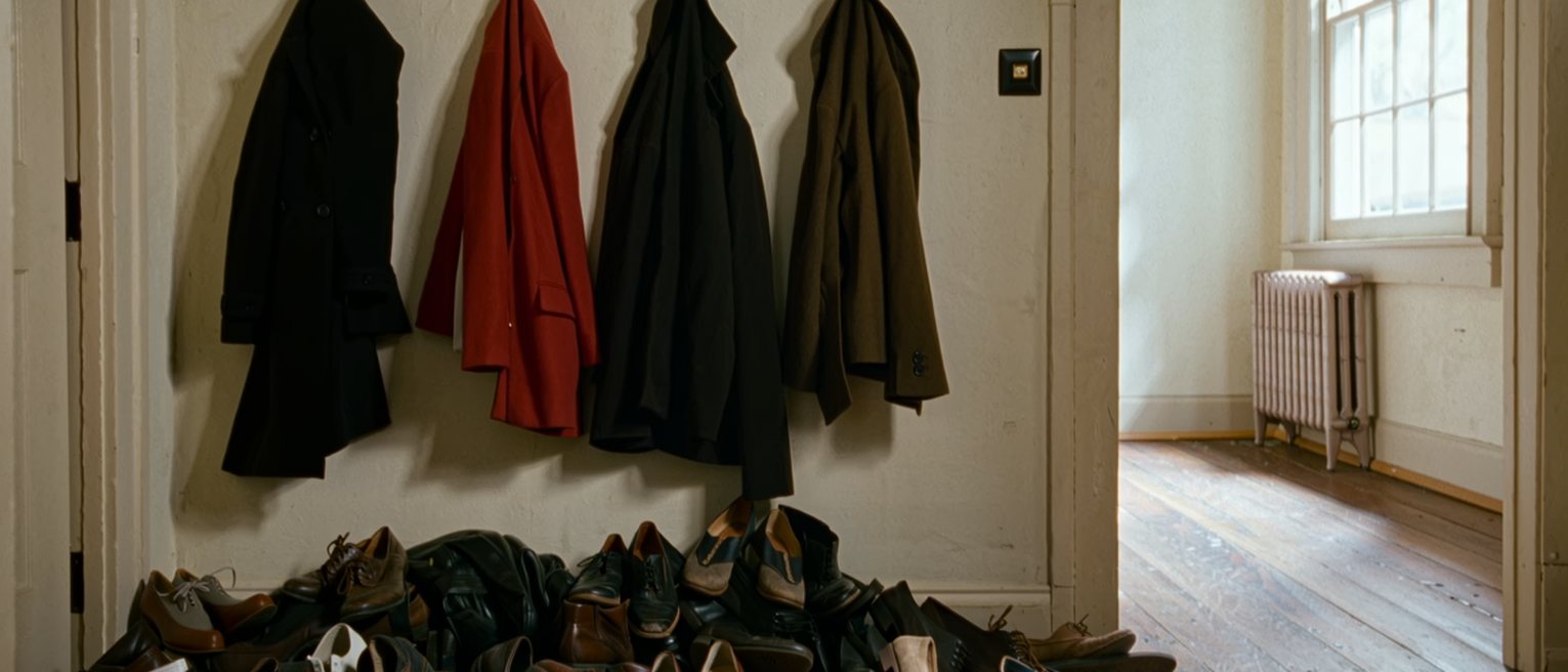 a hallway with four coats crowded onto five hooks and a heap of different shoes below them