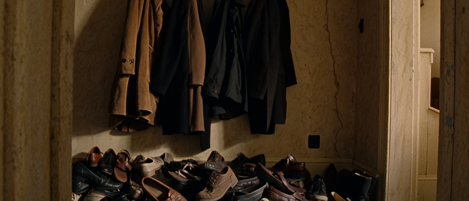 a hallway with four coats crowded onto five hooks and a heap of different shoes below them