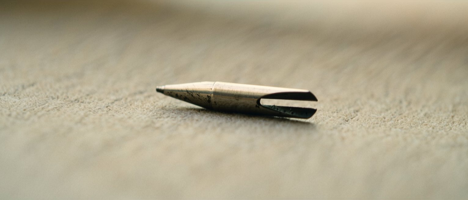 a steel pen nib with a split tip, its shoulders bright