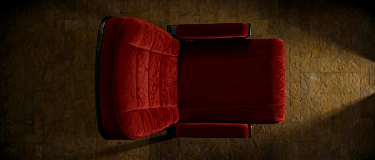 a single folded-up theatre seat of red plush with wooden armrests, standing alone at the end of a row of seats