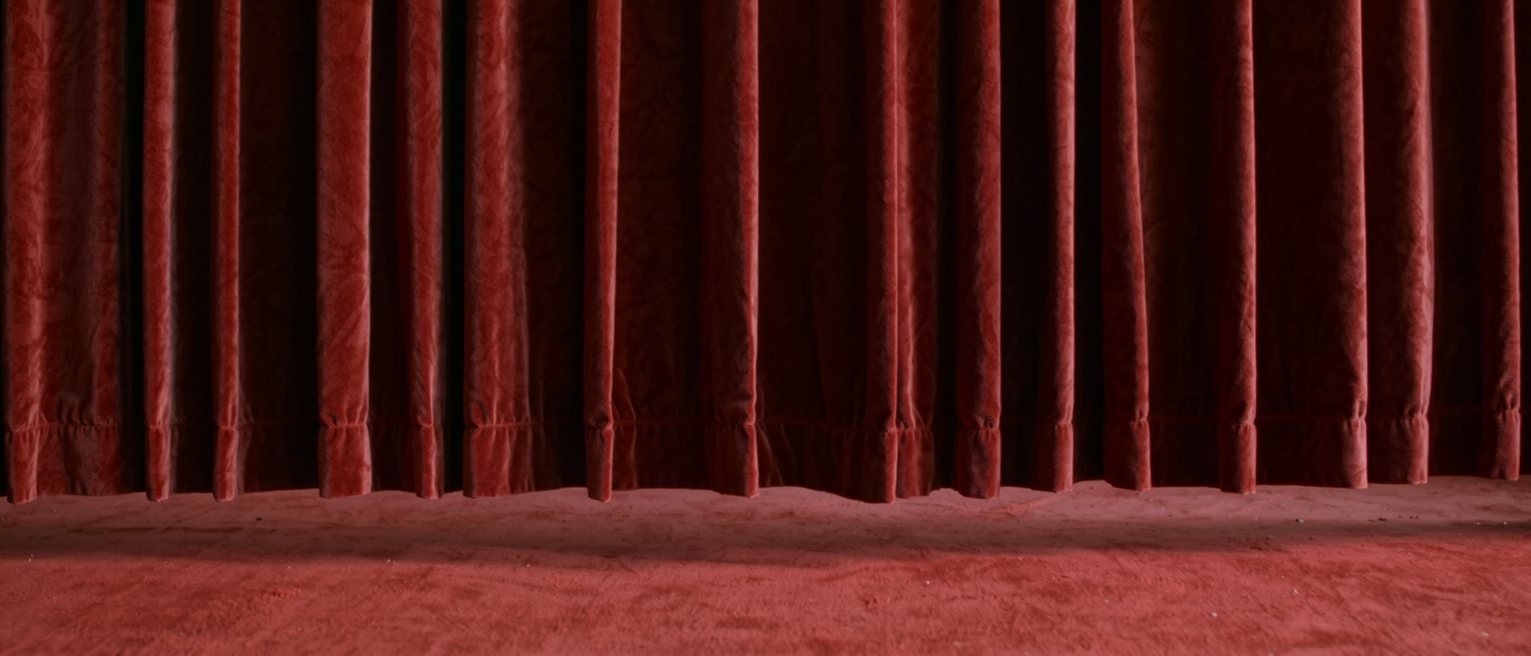 a heavy red velvet stage curtain hanging closed, the pleats falling straight
