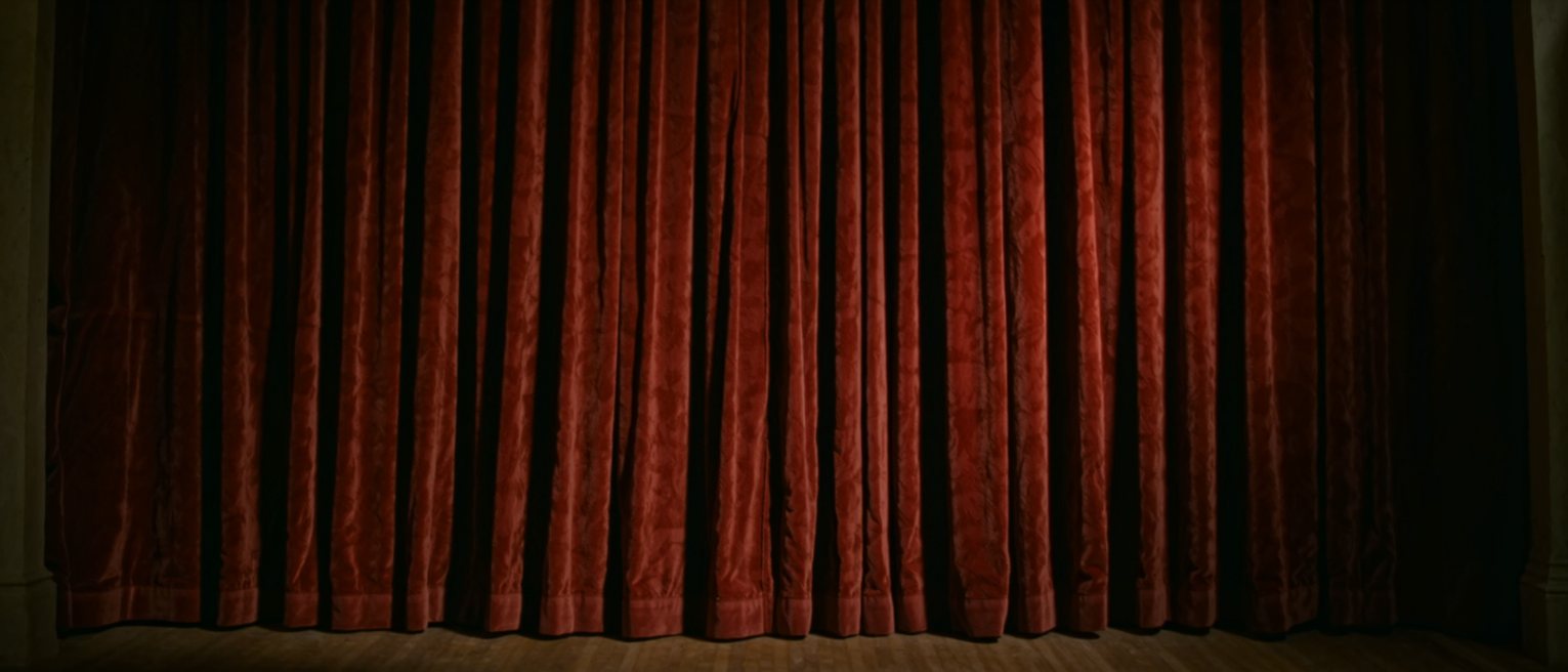 a heavy red velvet stage curtain hanging closed, the pleats falling straight