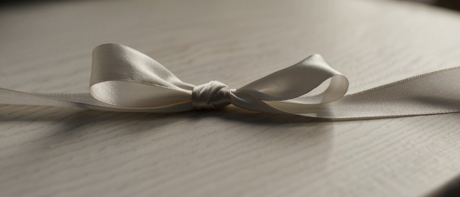 a length of silk ribbon tied in a single slipped bow on a bare table, one end left long