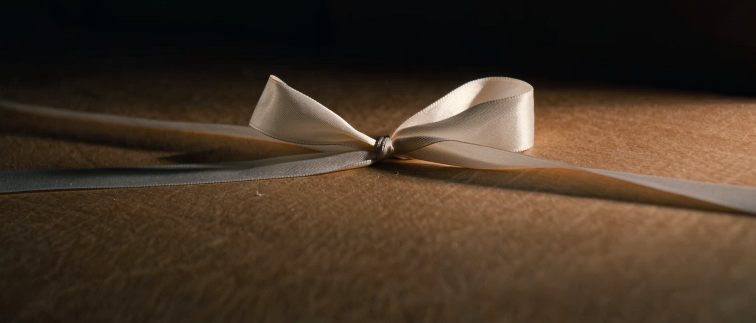 a length of silk ribbon tied in a single slipped bow on a bare table, one end left long