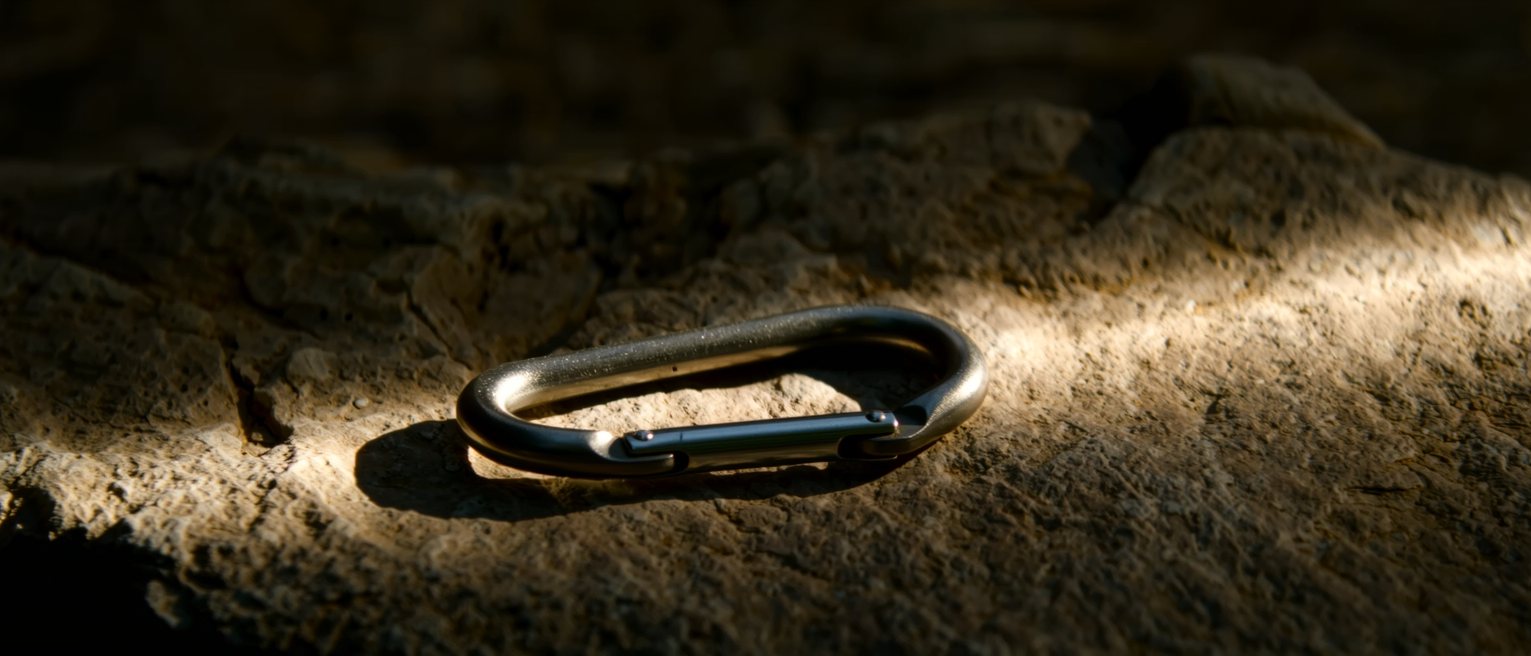 a steel climbing carabiner lying on rock, its sprung gate closed and the locking sleeve turned down