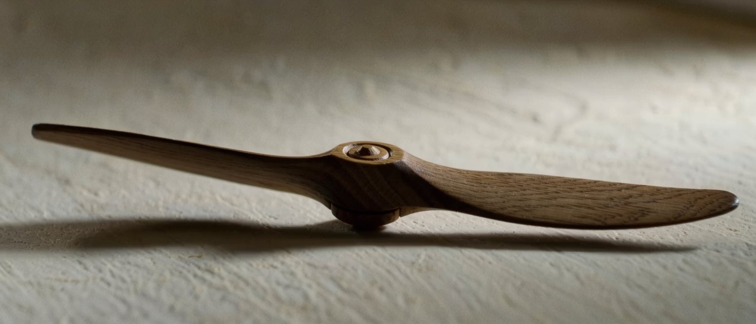 a carved wooden propeller lying on a bench, its blades true