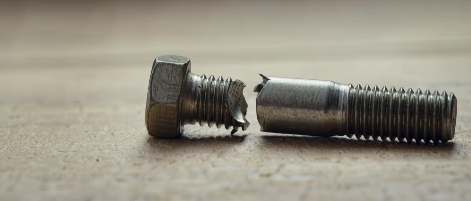 a snapped steel bolt and a bolt worn thin with use, lying side by side