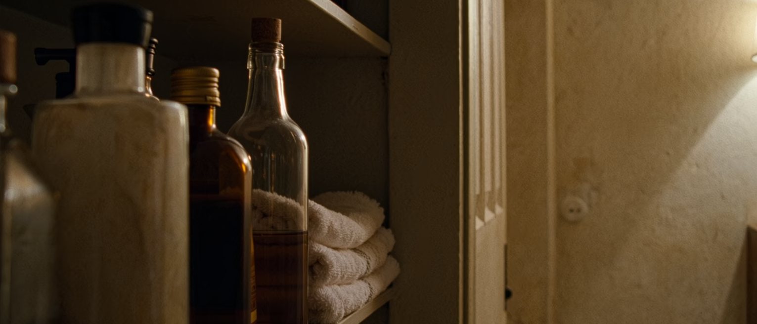 a bathroom shelf with a new bottle standing beside the old ones, its seal only just broken, a folded towel set ready underneath