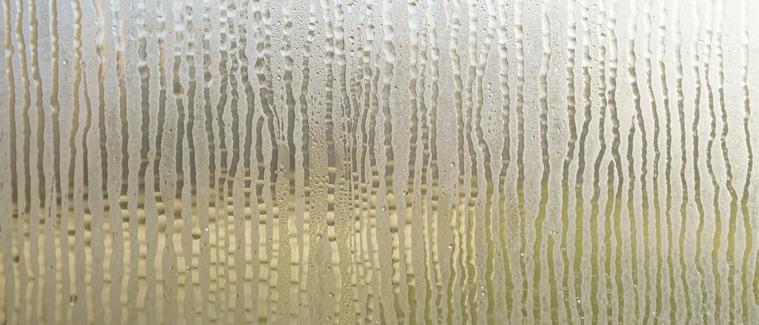a pane of old window glass fogged by breath, the condensation just beginning to bead and run