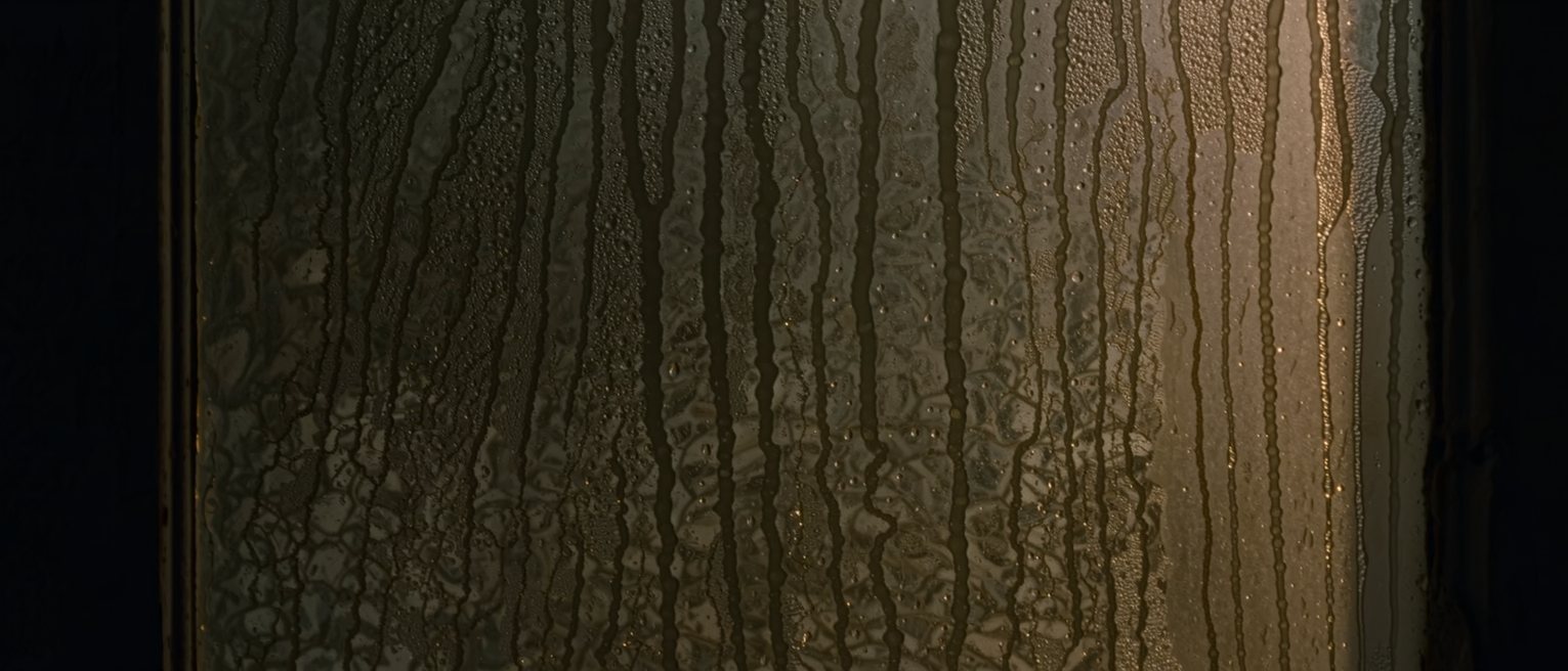 a pane of old window glass fogged by breath, the condensation just beginning to bead and run